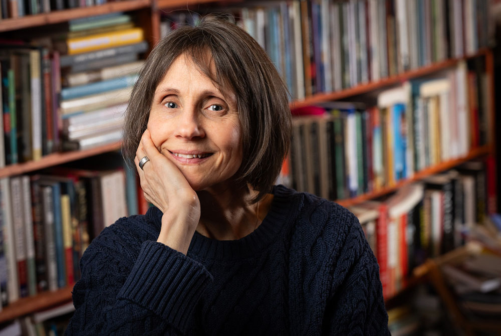 Photo: Joanna Lilley posing in front of rows of books on a bookcase