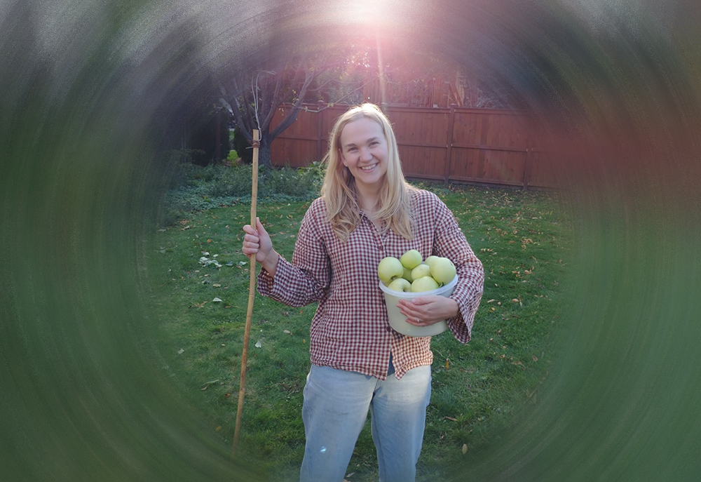 Photo: Sarah Ens holding a pail of green apples on a green lawn covered in fall leaves.